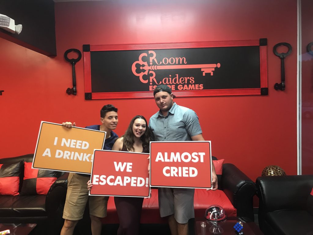 Three people holding signs in front of a red wall.