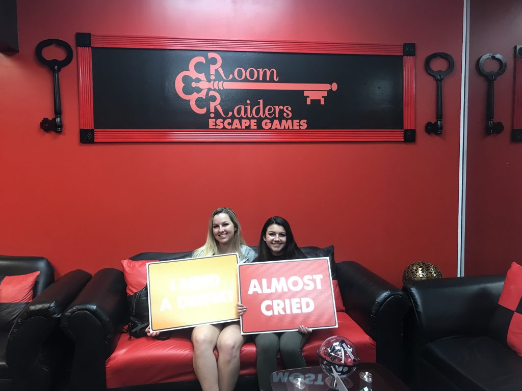Two women sitting on a red couch holding signs.