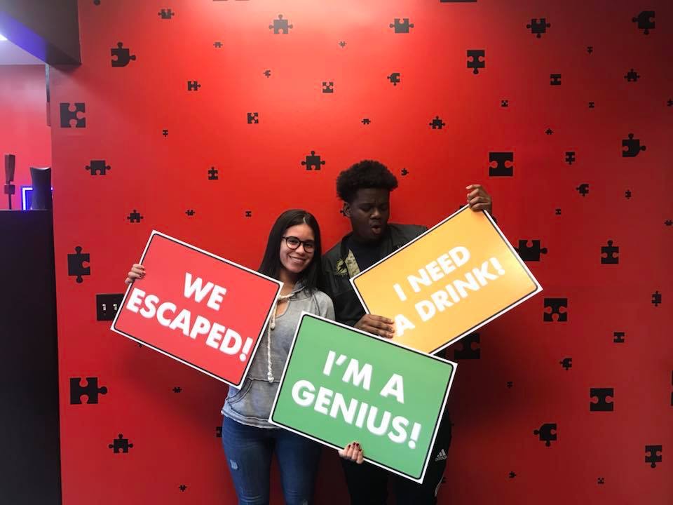 Two people holding signs in front of a red wall.