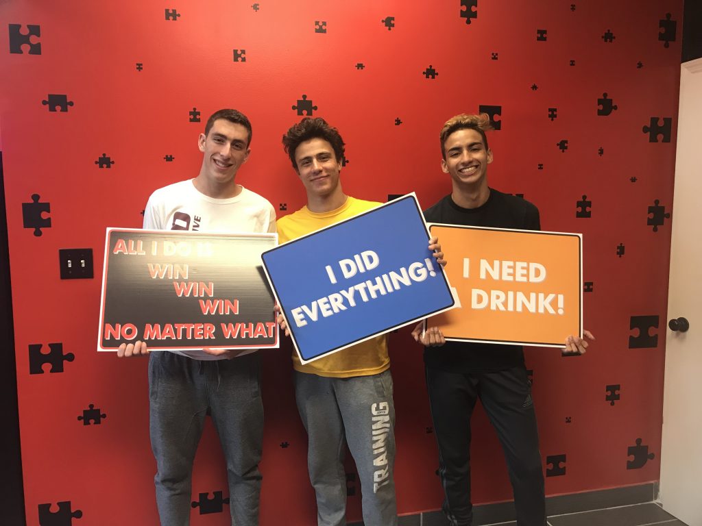 Three young men holding signs in front of a wall.