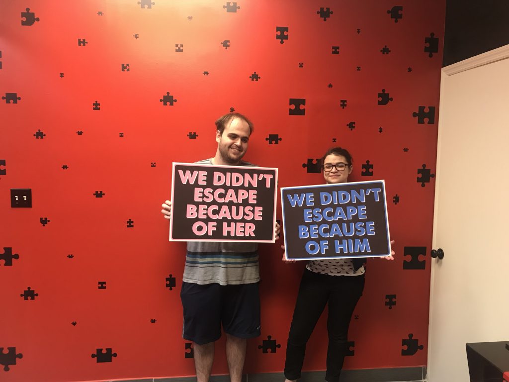 Two people holding signs in front of a wall.