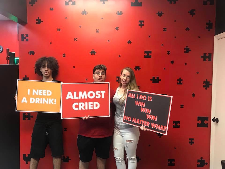 Three people holding signs in front of a red wall.