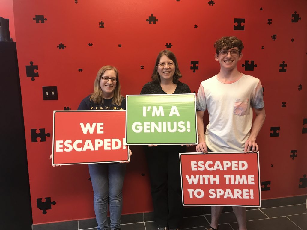 Three people holding signs in front of a red wall.