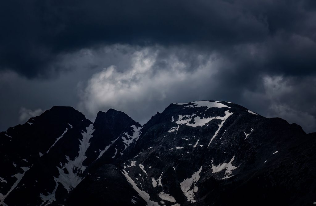 A mountain with snow on it and dark clouds above.